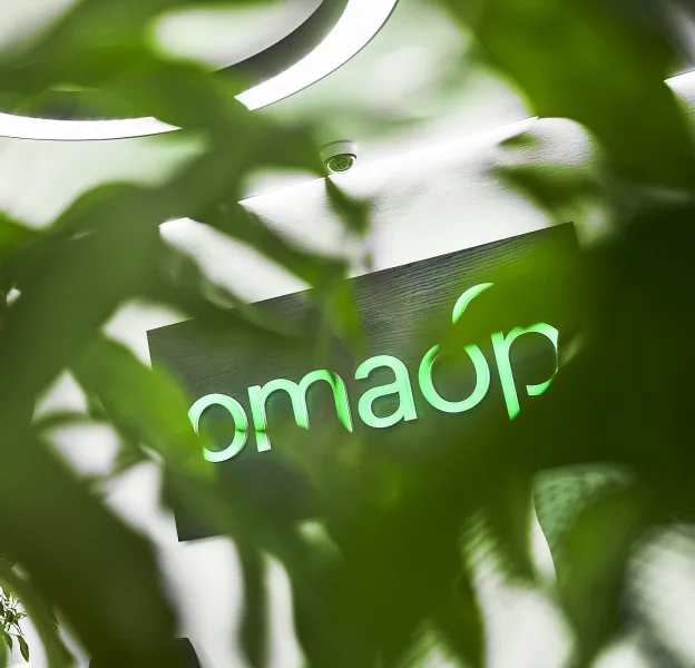Vihreiden lehtien takaa pilkistää OmaSp:n logo