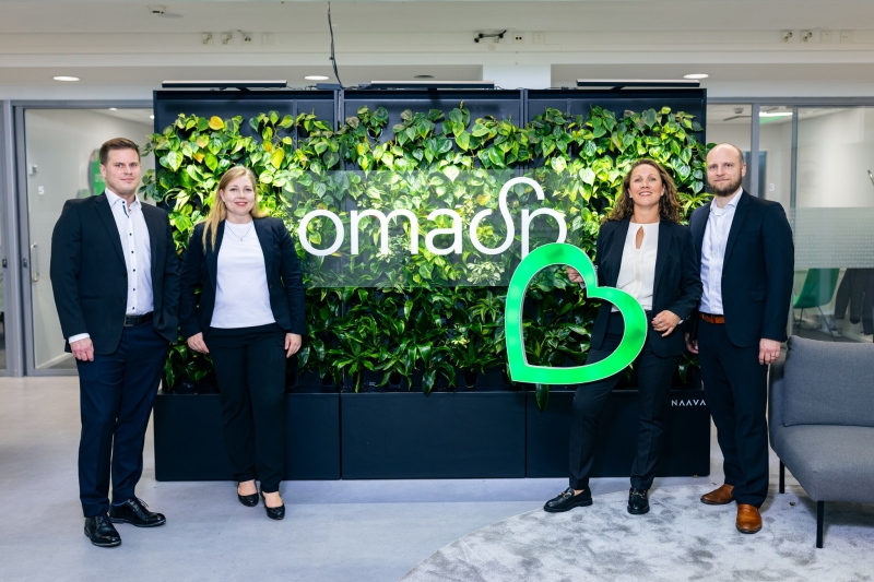 Neljä henkilöä seisoo kukkaseinän edessä, yhdellä vihreä valosydän käsissään.