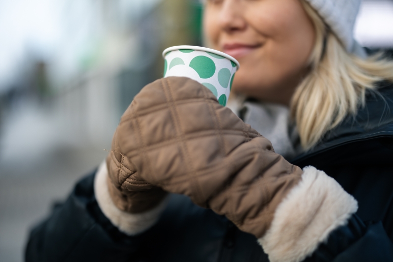 Henkilö juo kahvikupista ulkona ja hymyilee.