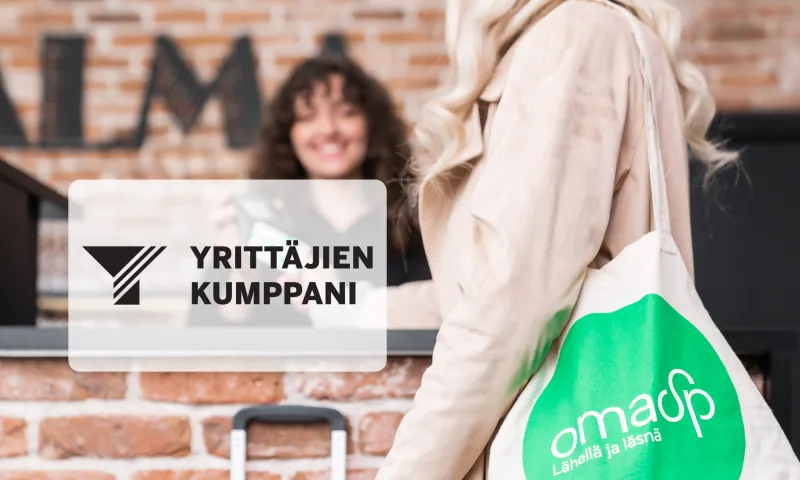 Nainen pankin kangaskassi olalla maksamassa hotellin vastaanotossa.