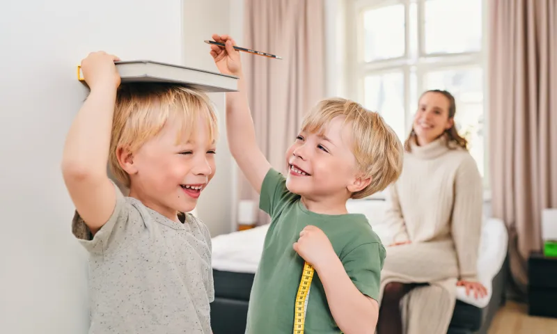 Lapset merkitsevät pituuksiaan seinälle äidin katsellessa.