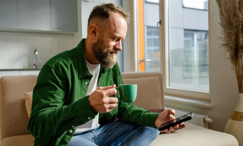 Henkilö selaamassa puhelinta kahvikuppi kädessään.