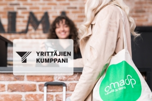 Nainen pankin kangaskassi olalla maksamassa hotellin vastaanotossa.