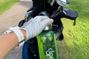 vihreä vesipullo, golfmailoja ja käsi, jossa valkoinen hansikas