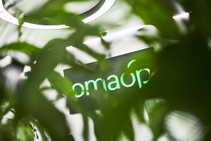 Vihreiden lehtien takaa pilkistää OmaSp:n logo
