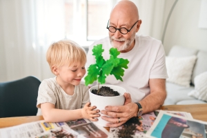 Isoisä ja lapsi istuttavat taimea ruukkuun.