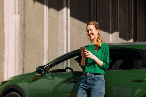 Nainen puhelimella nojailemassa autoon.