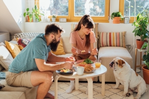 Pariskunta ja koira olohuoneessa aamiaisella.